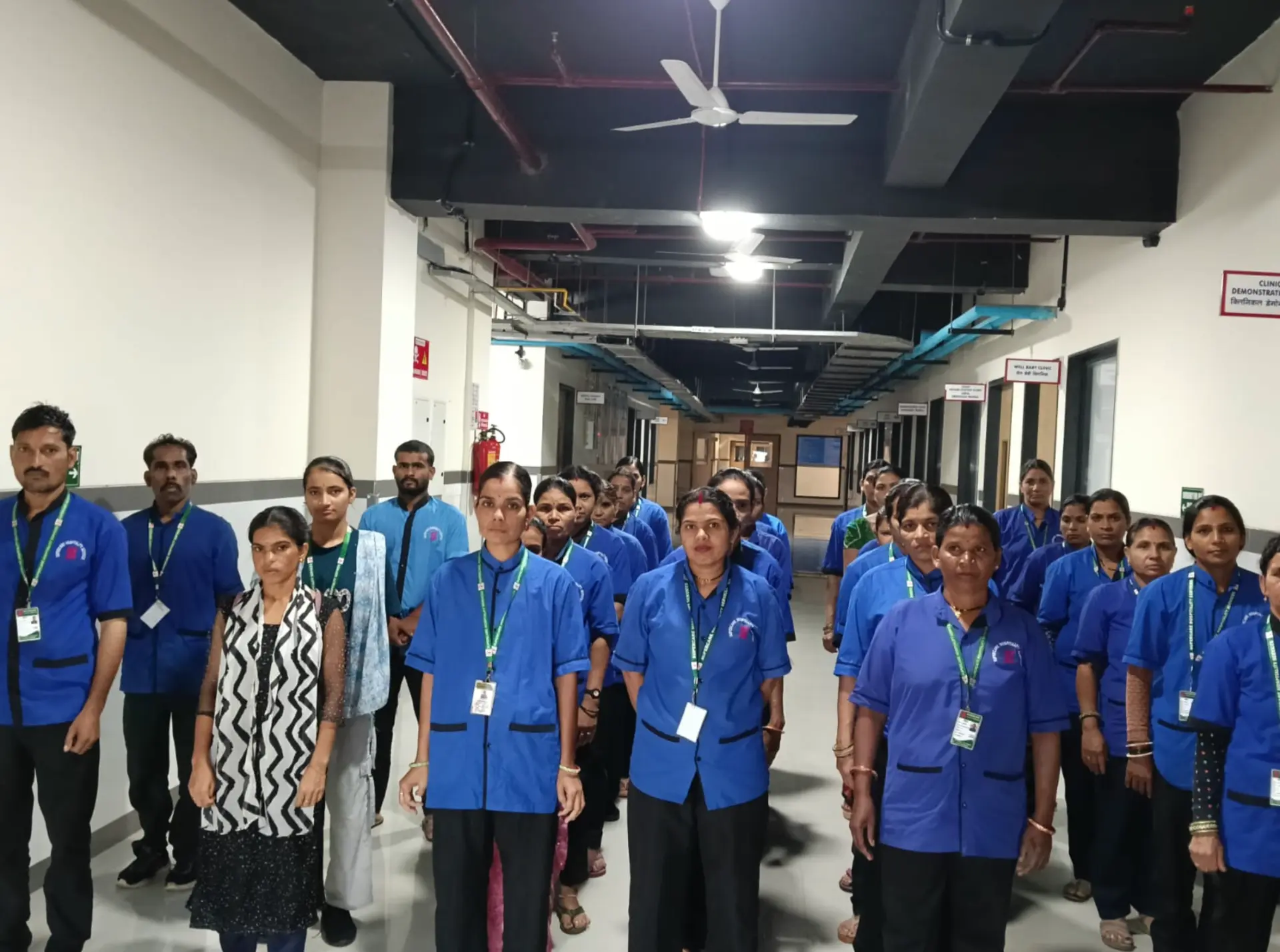Uniformed Supercare housekeeping team with ID cards lined up in a hospital corridor