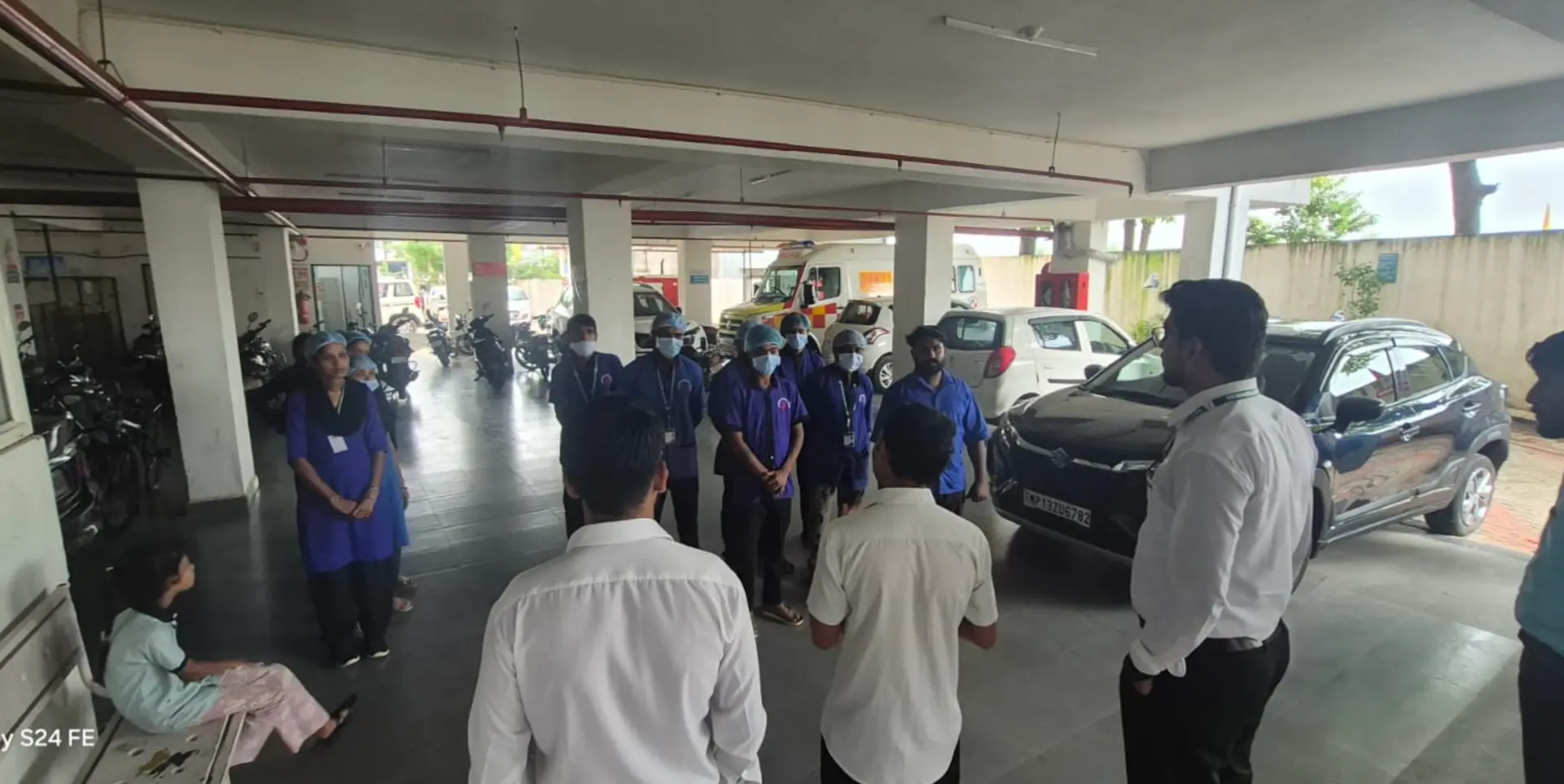 Supercare staff in masks and caps being briefed by supervisors at a hospital ambulance bay