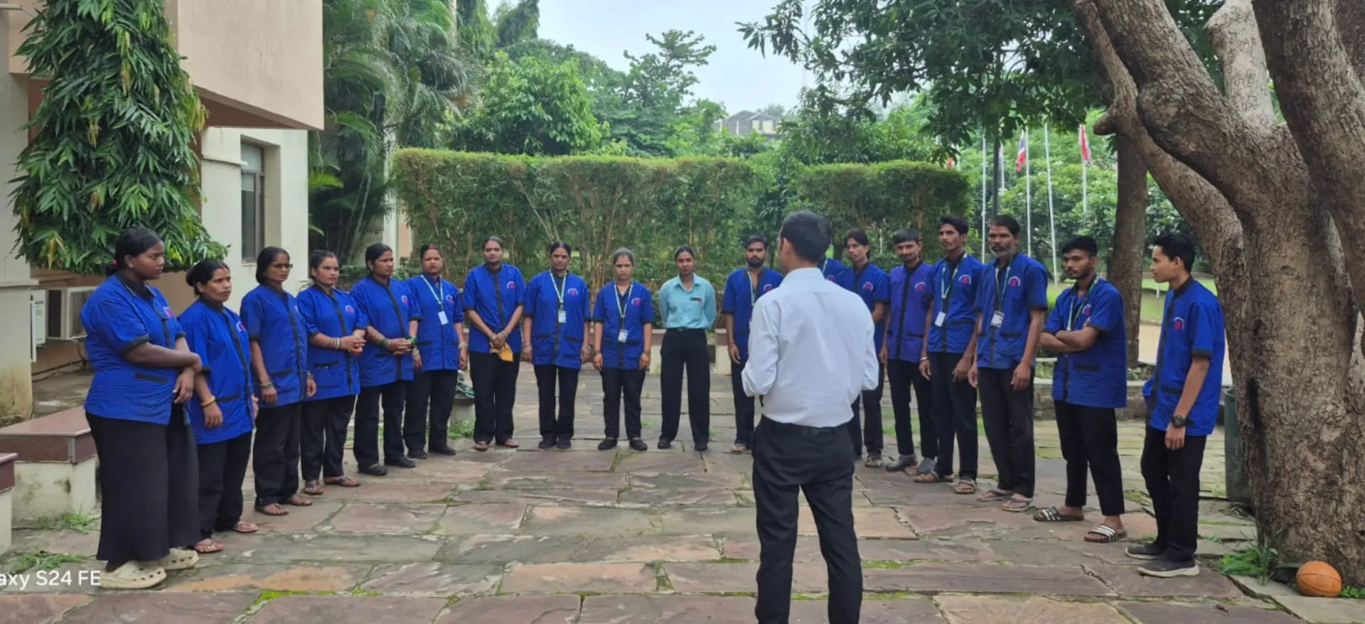 Supercare supervisor briefing uniformed housekeeping staff standing in a circle outdoors, ID lanyards visible